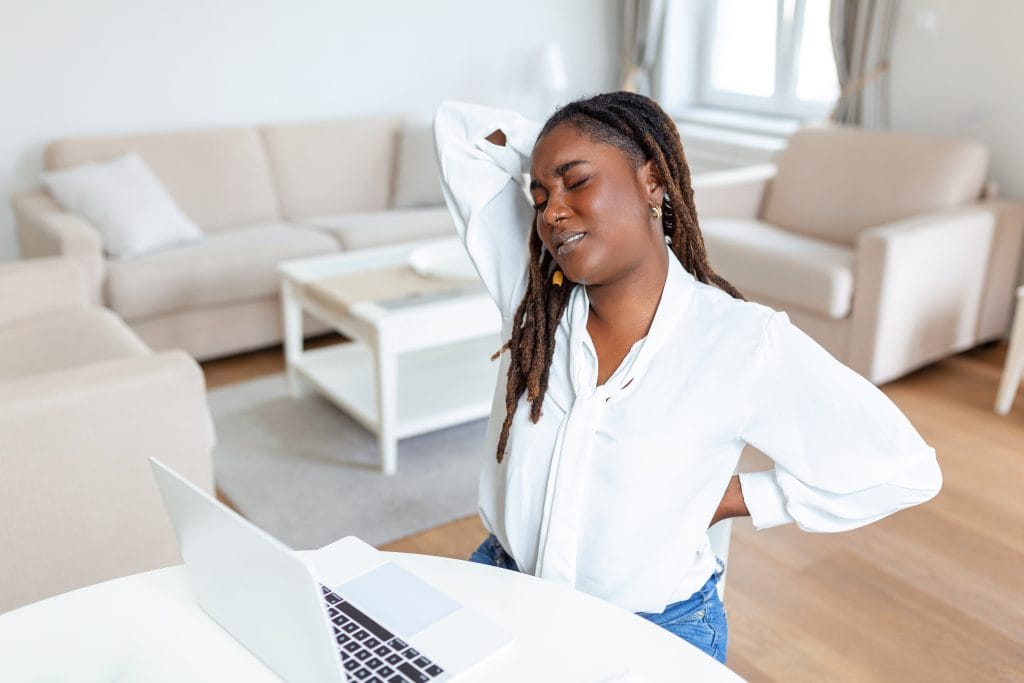 Woman working from home at her laptop holding her stiff neck and lower back after sitting at a desk all day
