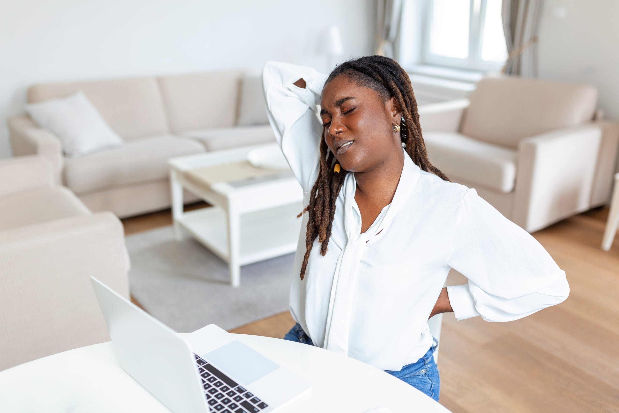 Woman working from home at her laptop holding her stiff neck and lower back after sitting at a desk all day